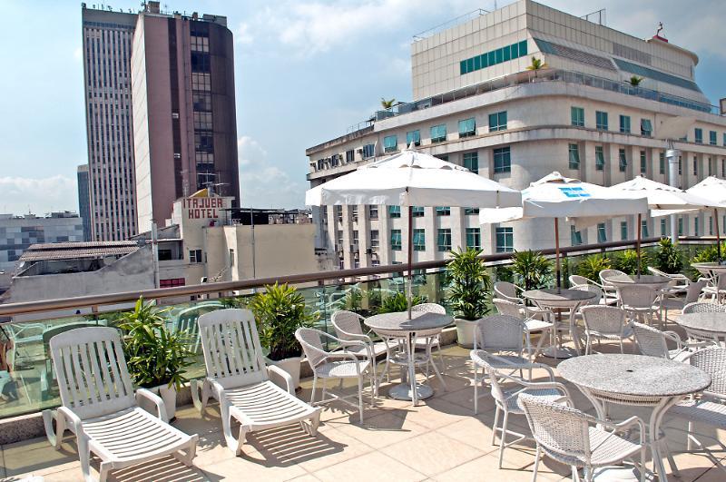 Hotel Atlantico Business Centro Rio de Janeiro Eksteriør bilde The photo shows a rooftop area with several white lounge chairs and circular tables. There are umbrellas providing shade over some of the seating. In the background, there are tall buildings, including a modern skyscraper with a distinct architectura